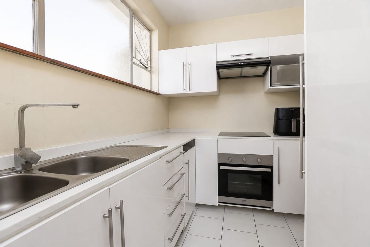 A clean, modern kitchen featuring white cabinetry, stone countertops, stainless steel sink, and integrated appliances including an oven, hob, and extractor fan.