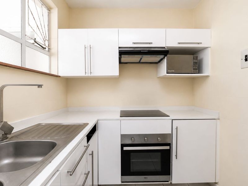 A clean, compact kitchen featuring white cabinetry, a stainless steel sink, built-in oven, electric hob, and an integrated extractor fan.