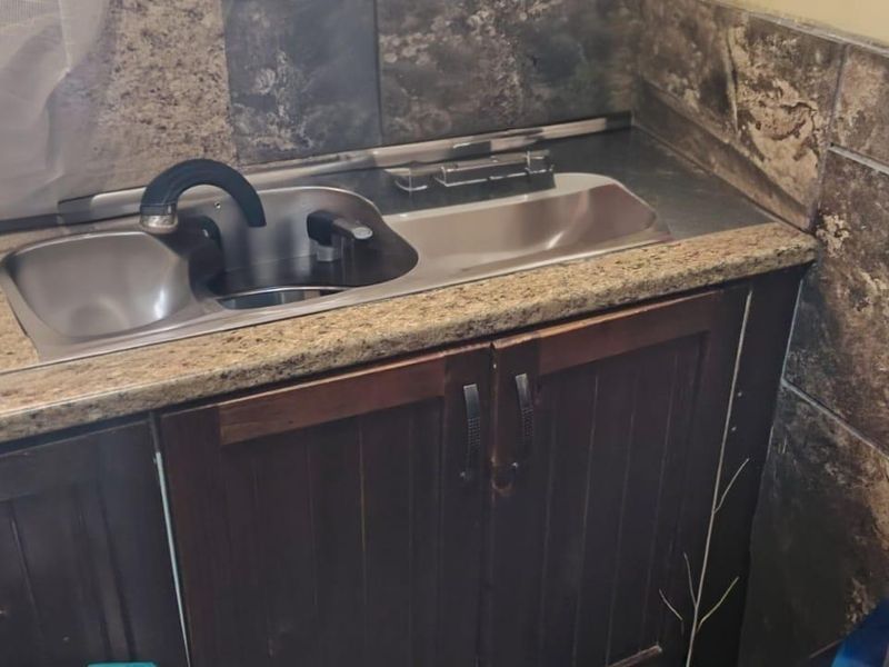 A compact kitchen area featuring dark wood cabinetry, a granite countertop, and a stainless steel double sink with a tiled backsplash.