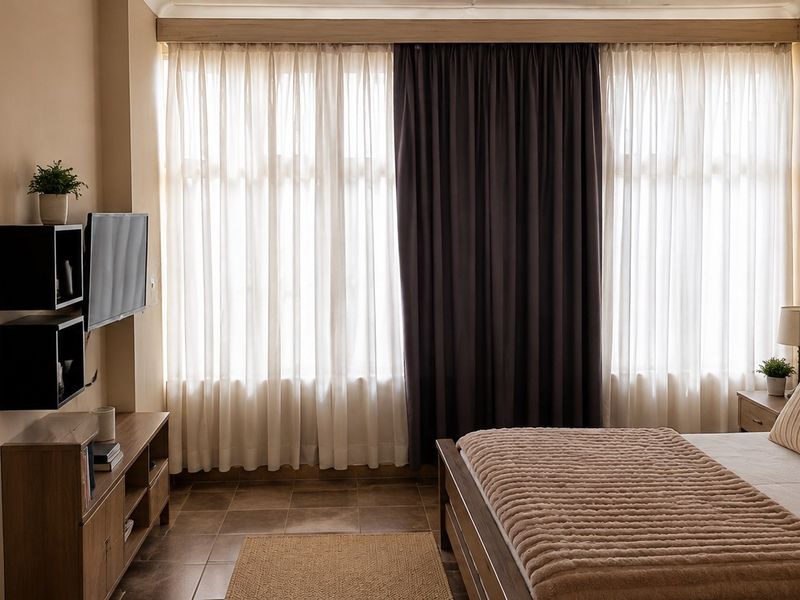 A well-lit bedroom featuring tiled flooring and large windows with layered curtains, creating a warm and inviting atmosphere.