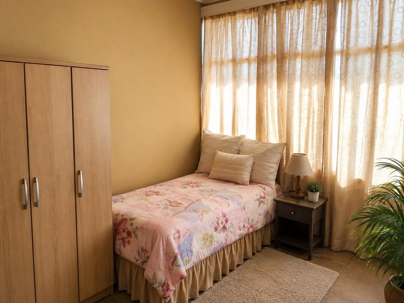 A cozy bedroom featuring tiled flooring, a built-in wardrobe, and large windows with natural light.