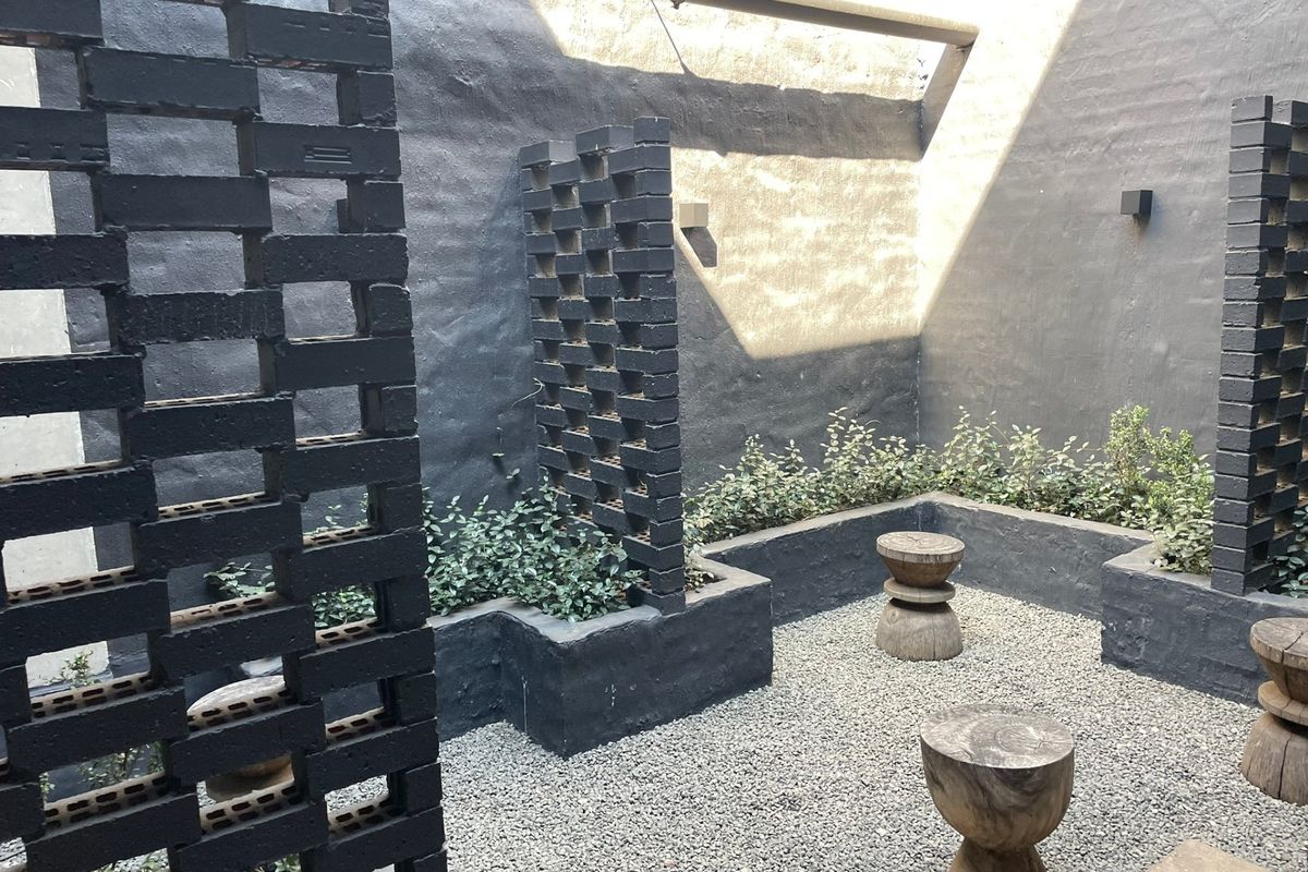 A modern, low-maintenance rear courtyard featuring dark-painted brick privacy screens, raised masonry garden beds, and gravel surfacing.