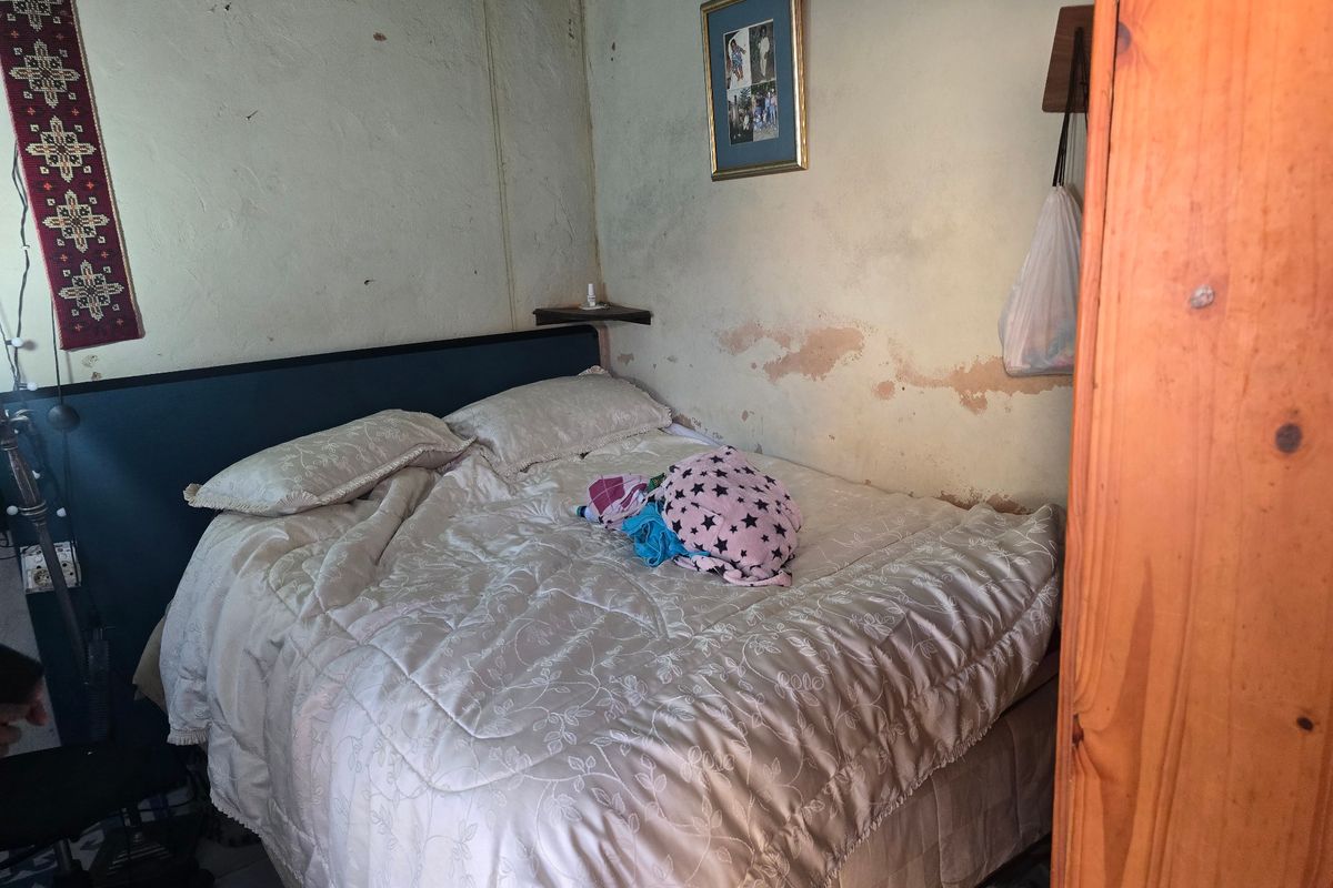 A bedroom featuring a built-in headboard, currently showing significant wall surface deterioration and peeling paint requiring maintenance.