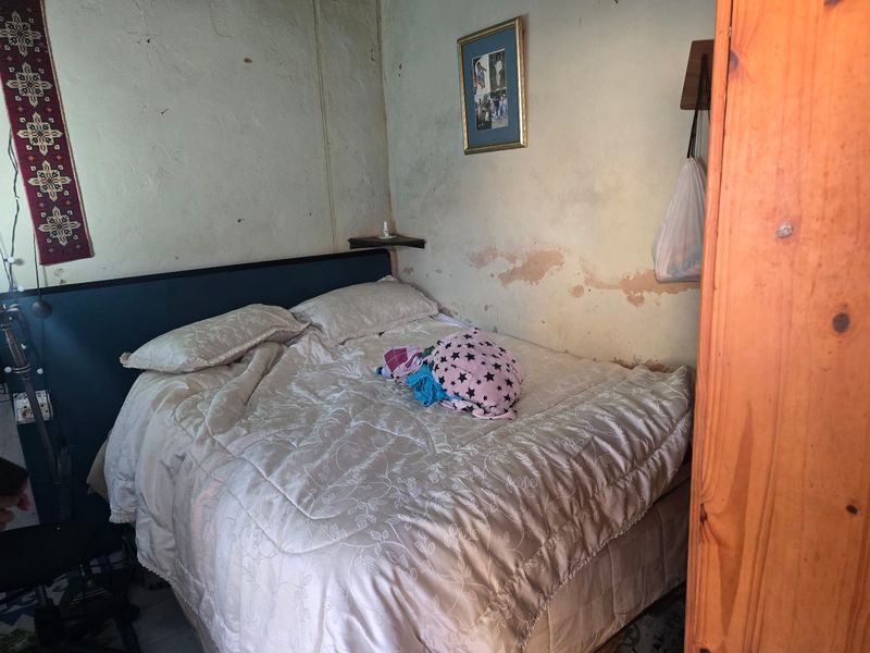 A bedroom featuring a built-in headboard, currently showing significant wall surface deterioration and peeling paint requiring maintenance.