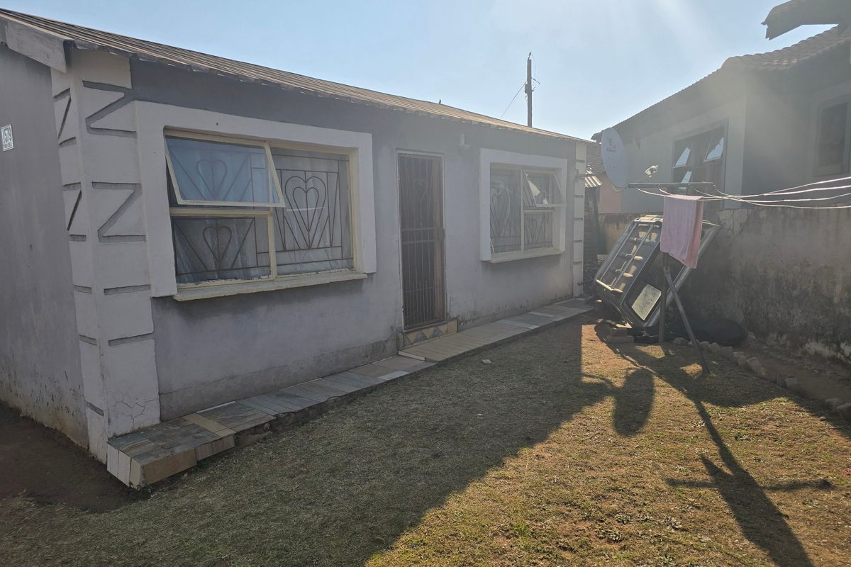 Rear view of the property featuring a small garden area, tiled walkway, and security bars on the windows.