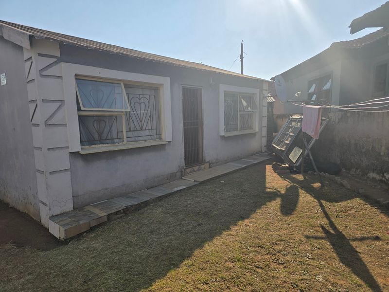 Rear view of the property featuring a small garden area, tiled walkway, and security bars on the windows.