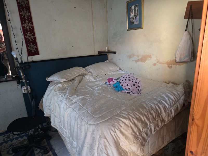 A bedroom featuring a built-in headboard and wall-mounted shelving, currently requiring significant wall surface repairs and cosmetic updates.