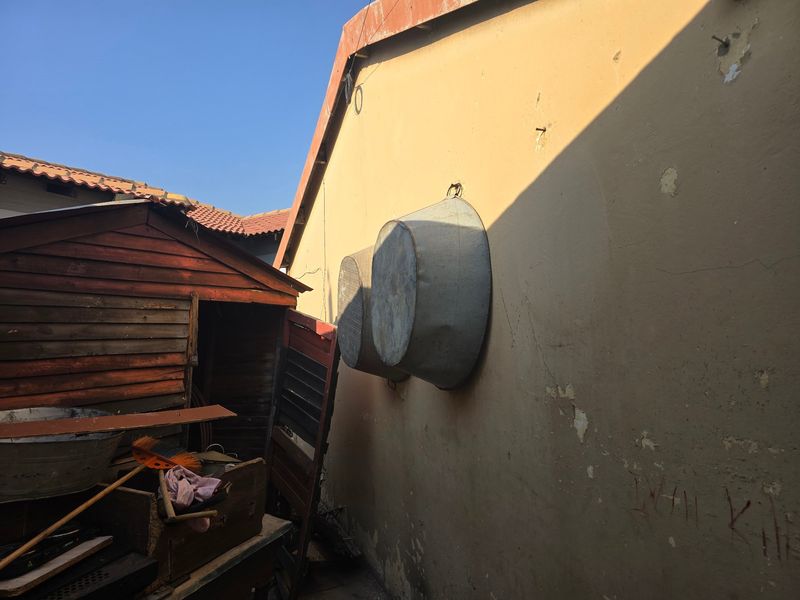 Rear exterior view showing a weathered timber shed and a plastered wall with visible signs of paint deterioration and surface damage.