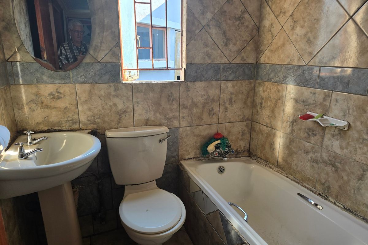 A dated bathroom featuring a pedestal basin, toilet, and bathtub with tiled walls. The space requires renovation to update finishes and address tile damage.