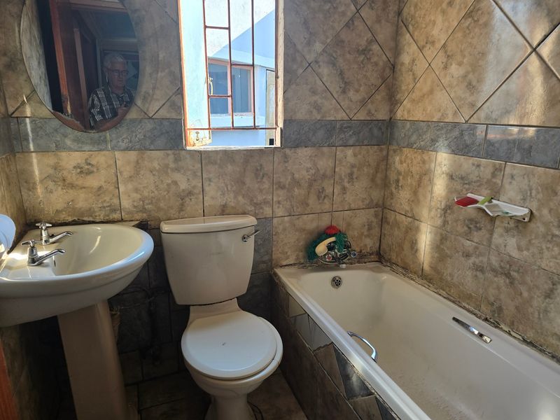 A dated bathroom featuring a pedestal basin, toilet, and bathtub with tiled walls. The space requires renovation to update finishes and address tile damage.