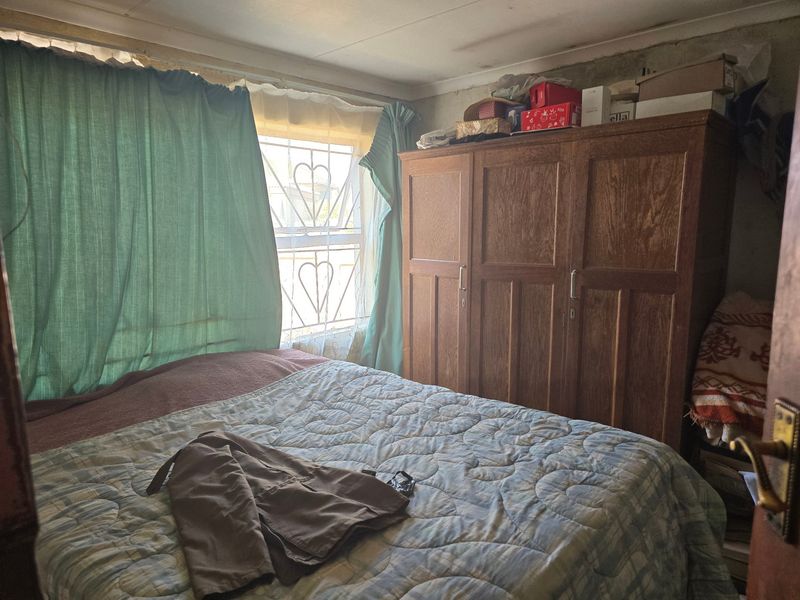 A bedroom featuring a built-in wardrobe and security gate on the window, requiring cosmetic updates to the ceiling and wall finishes.