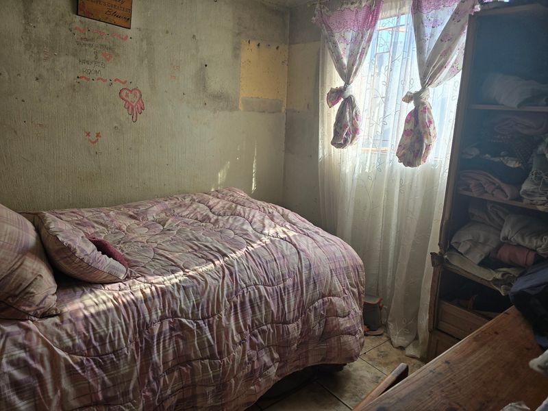 A bedroom featuring tiled flooring and a window, currently requiring significant wall repairs and cosmetic updates to improve the overall condition.