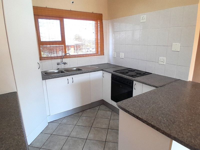 A functional kitchen featuring white cabinetry, dark laminate countertops, a built-in oven with electric hob, and tiled flooring.