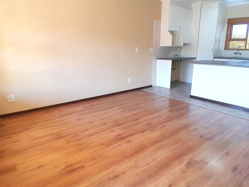 An open-plan living area featuring laminate flooring and an adjoining kitchen space with built-in cabinetry and sink.