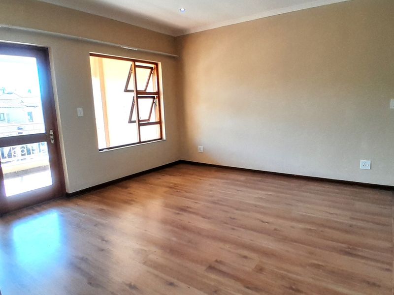 A bright, empty living room featuring modern laminate flooring, recessed downlights, and a glass door leading to an outdoor area.