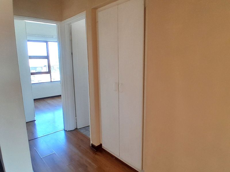 A clean, empty hallway featuring laminate flooring and a built-in storage cupboard, providing access to adjacent rooms.