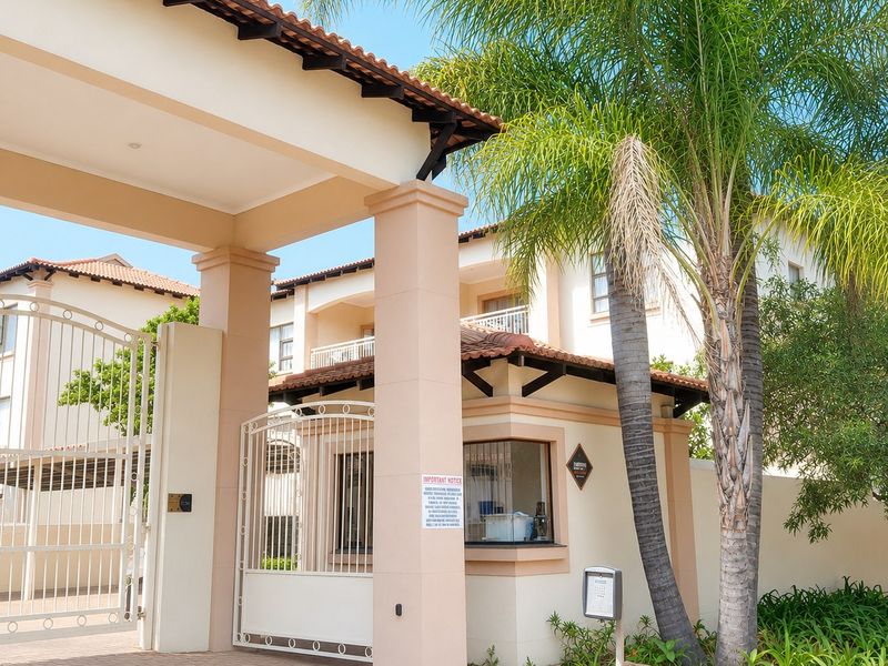 Secure apartment complex entrance featuring a gated access point, guard house, and paved driveway with well-maintained exterior finishes.