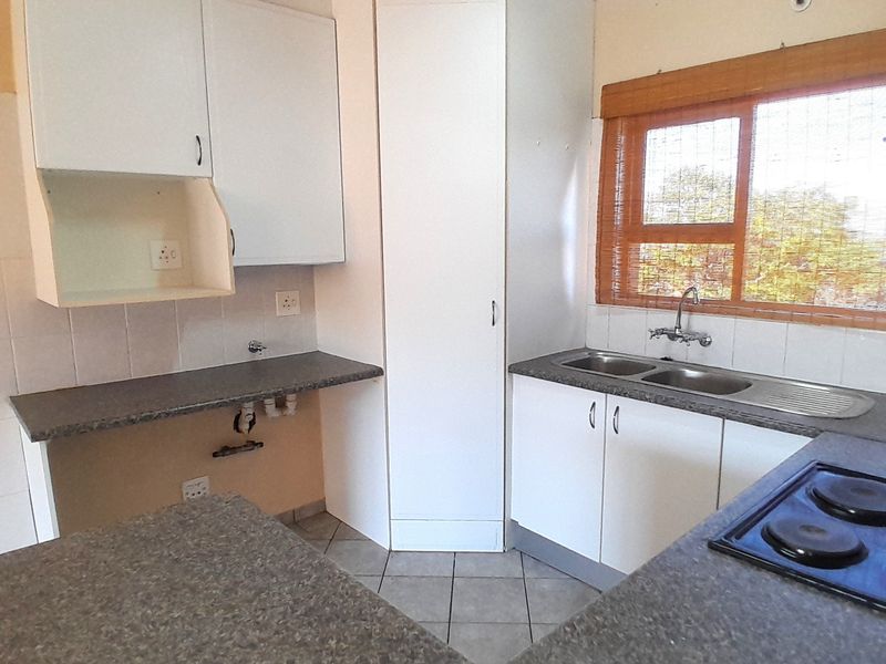 A functional kitchen featuring white cabinetry, laminate countertops, a double stainless steel sink, and an integrated electric hob with tiled splashbacks.