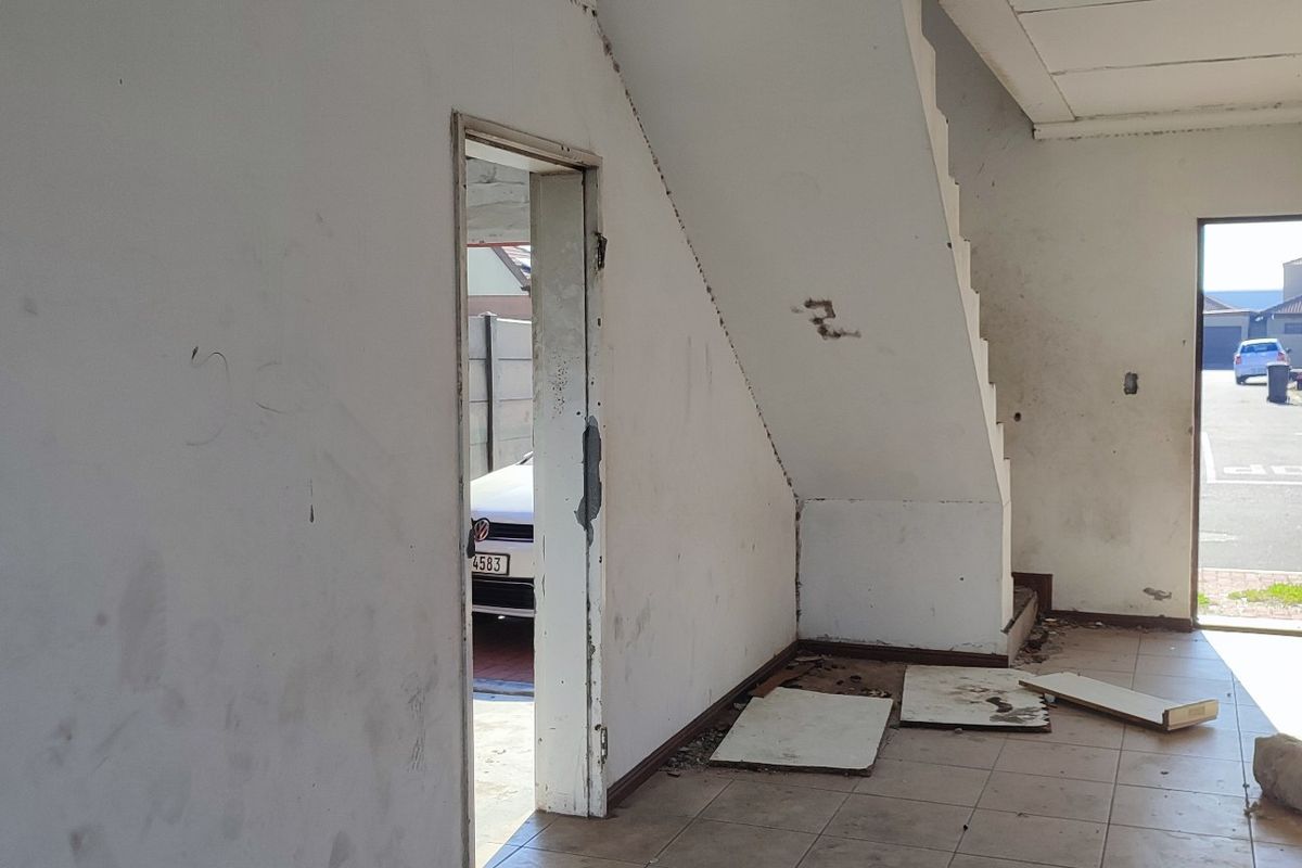 An empty, unfinished living area featuring a staircase, tiled flooring, and direct access to the exterior, requiring cosmetic renovation and finishing touches.