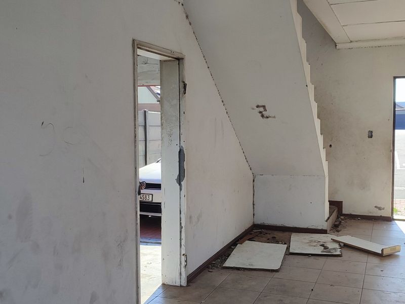 An empty, unfinished living area featuring a staircase, tiled flooring, and direct access to the exterior, requiring cosmetic renovation and finishing touches.