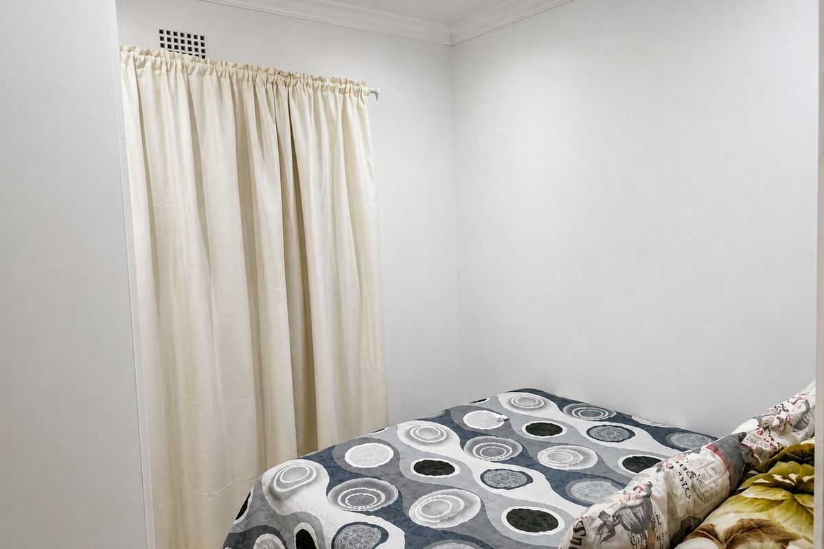 A simple bedroom featuring white walls, crown molding, and a ventilation grille, providing a clean and neutral space.
