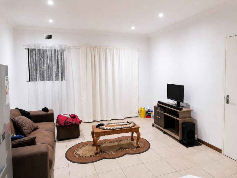 A functional living room featuring neutral tiled flooring, recessed downlighting, and clean white walls, providing a versatile space for relaxation.