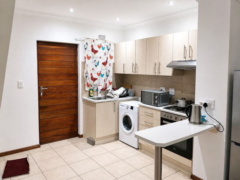 A functional kitchen featuring light wood cabinetry, tiled flooring, built-in oven and hob, and a convenient breakfast bar counter.