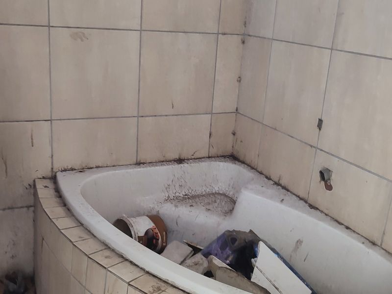 A bathroom featuring a built-in bathtub with tiled surround, currently in poor condition and requiring significant cleaning and renovation.