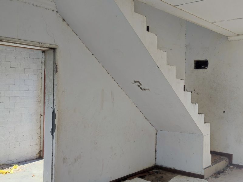 An empty, unfinished living area featuring a staircase, exposed wall sections, and direct access to the exterior, offering a blank canvas for renovation.