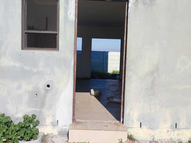 Rear exterior view of the property showing a tiled entrance, weathered plaster walls, and a concrete boundary wall in the background.
