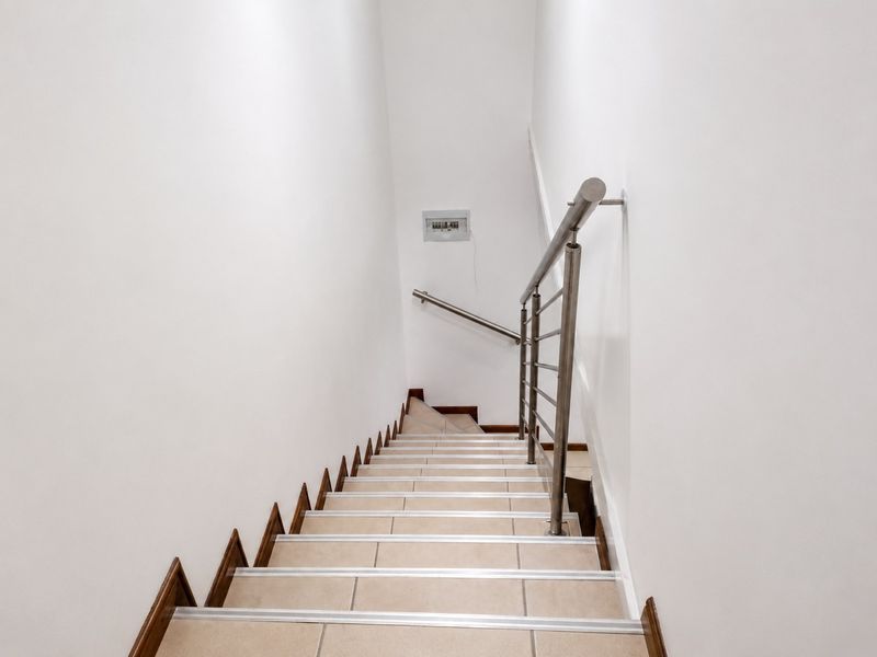 A clean, well-lit staircase featuring tiled steps and a modern stainless steel handrail, providing access between levels.