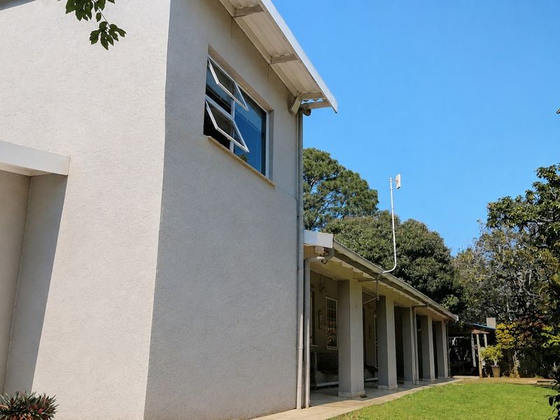 Rear view of the property featuring a covered patio area with concrete columns, casement windows, and a well-maintained lawn.