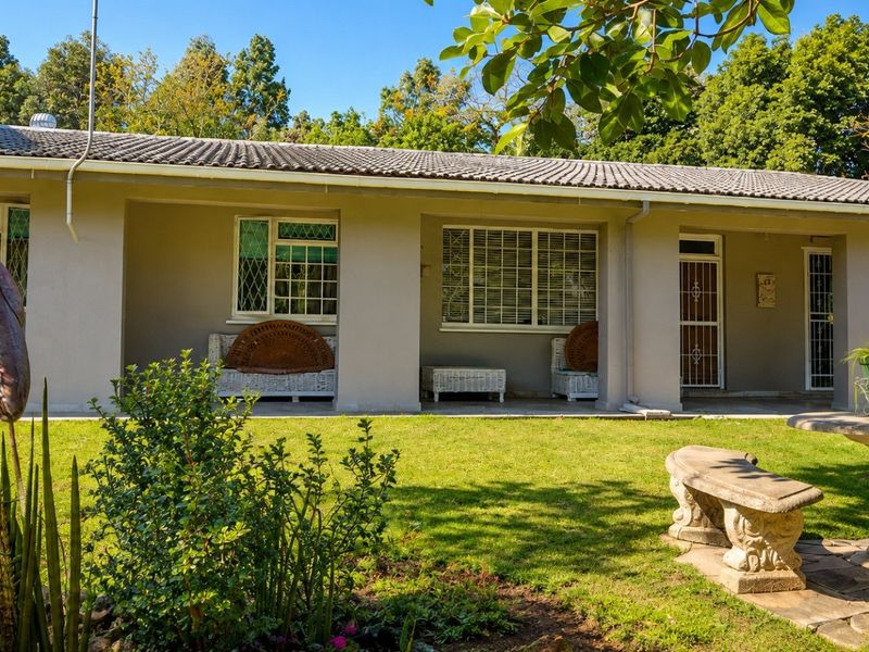 A well-maintained rear exterior view featuring a covered patio, tiled roof, and secure window treatments overlooking a landscaped garden area.