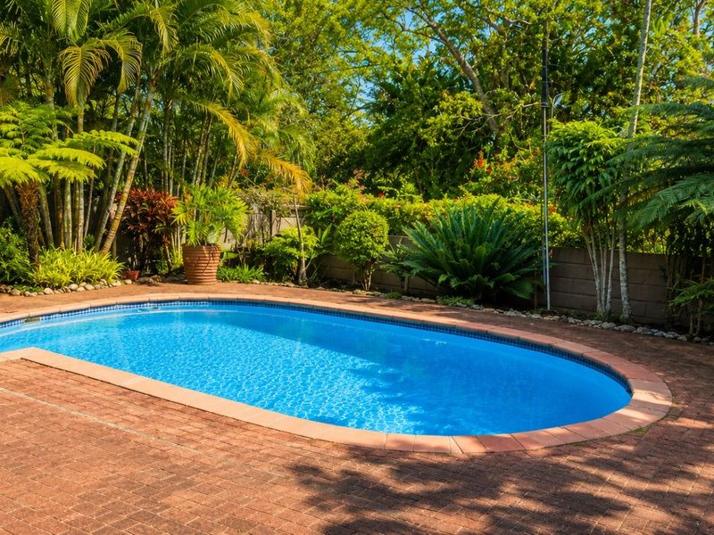 A well-maintained swimming pool area featuring brick paving and lush, established garden landscaping, providing a private and tranquil outdoor setting.