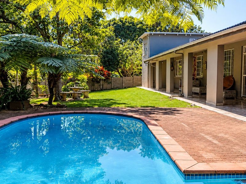 A well-maintained outdoor area featuring a swimming pool, brick-paved surround, and a covered patio extending from the main house structure.