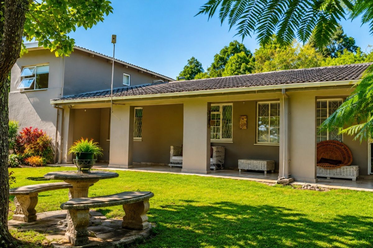 A well-maintained rear exterior view featuring a covered patio, tiled roof, and a spacious garden area with established trees.