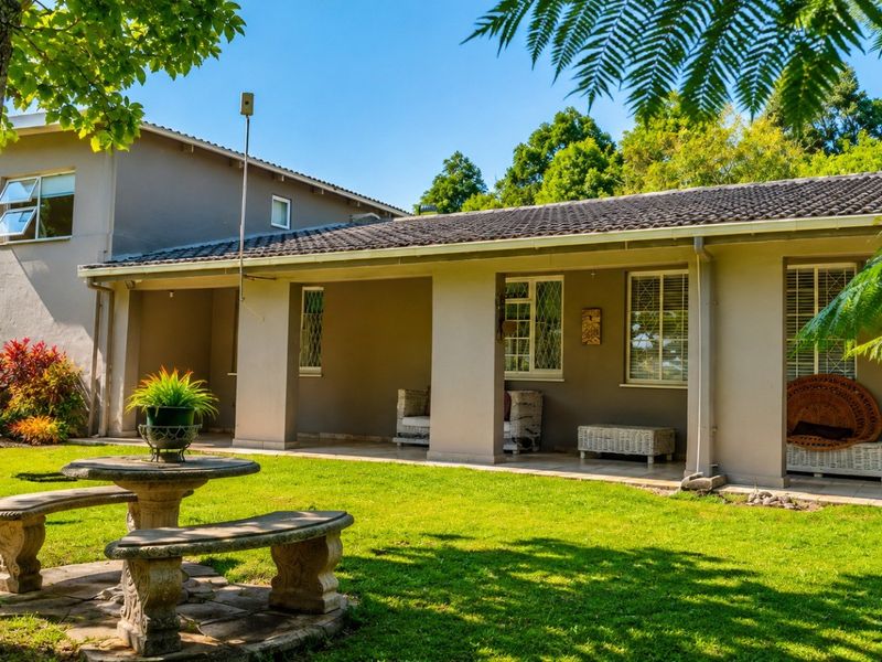 A well-maintained rear exterior view featuring a covered patio, tiled roof, and a spacious garden area with established trees.