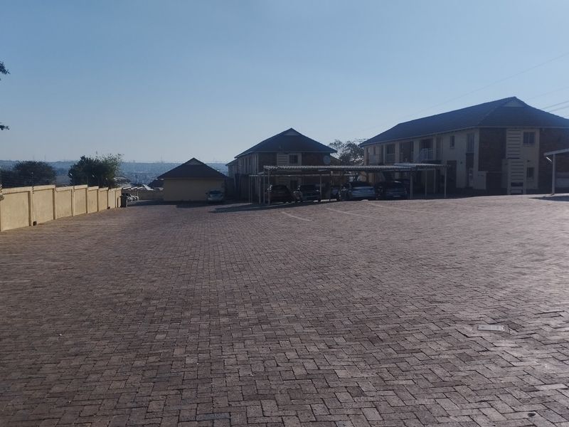 Spacious paved parking area and driveway serving the townhouse complex, featuring covered carport structures and perimeter security walling.