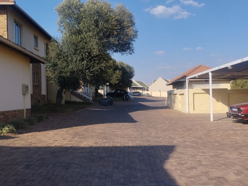 A view of the townhouse complex driveway featuring paved surfaces and covered carport parking structures.