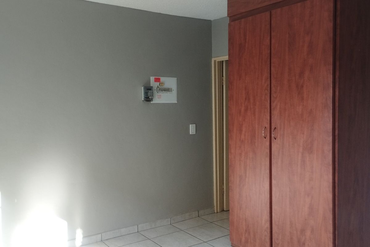 A clean, empty bedroom featuring tiled flooring, a built-in wooden wardrobe, and neutral grey walls.