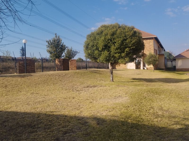 A view of the communal garden area featuring a lawn, mature tree, and secure perimeter fencing with brick pillars.