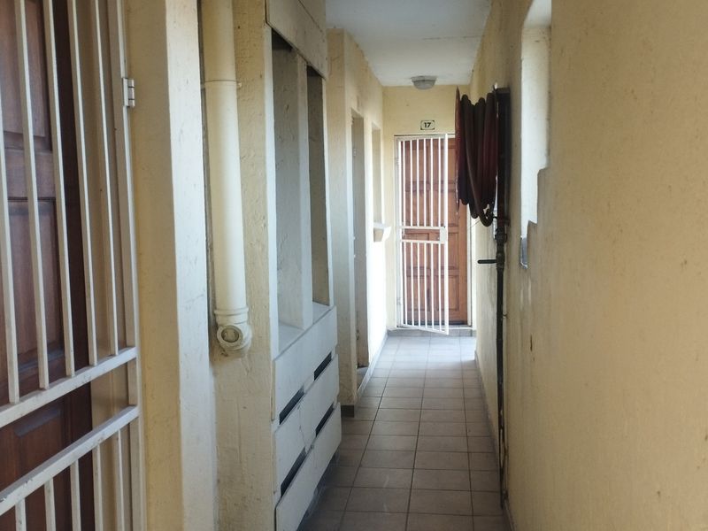 A functional outdoor-facing hallway featuring tiled flooring, a security gate, and a wall-mounted fire hose reel.