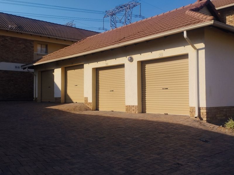A row of four secure roll-up garages with a brick-paved driveway in a well-maintained townhouse complex.