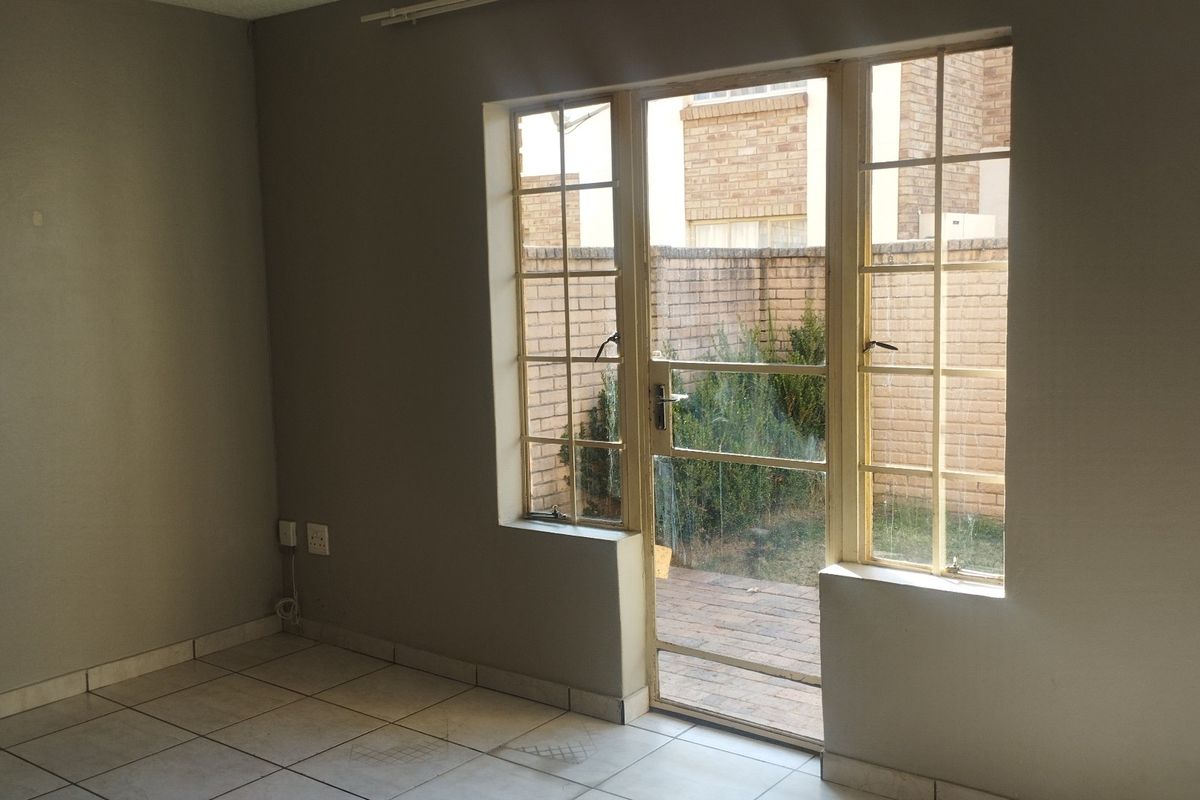 An empty living room featuring tiled flooring and a glass door providing direct access to a private rear courtyard area.