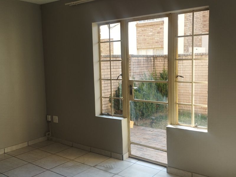 An empty living room featuring tiled flooring and a glass door providing direct access to a private rear courtyard area.