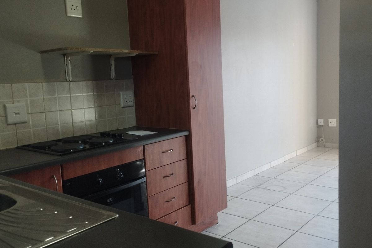 A functional kitchen area featuring built-in cabinetry, an electric hob, an oven, and tiled flooring, offering a clean and practical layout.