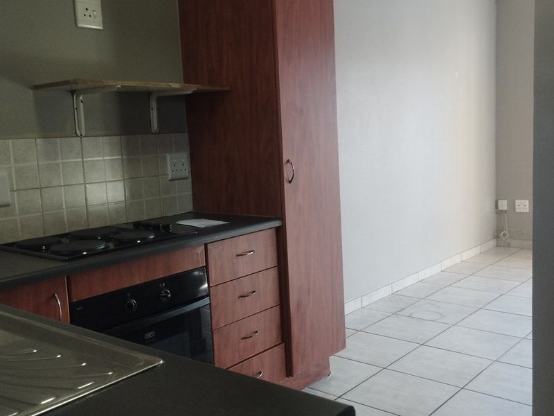 A functional kitchen area featuring built-in cabinetry, an electric hob, an oven, and tiled flooring, offering a clean and practical layout.