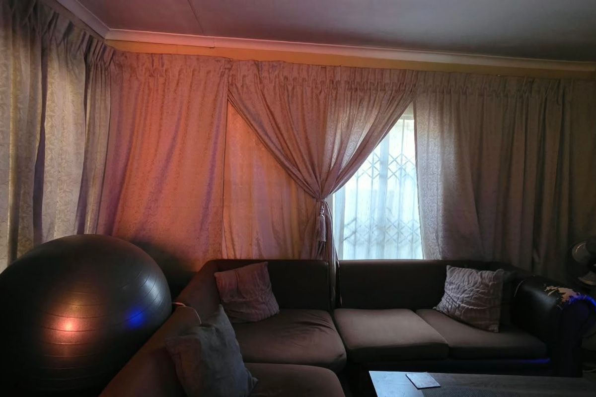 A living room area featuring a window with security gate and decorative coving, currently used as a lounge space.