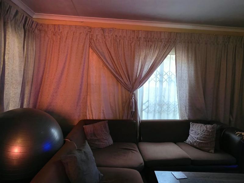 A living room area featuring a window with security gate and decorative coving, currently used as a lounge space.