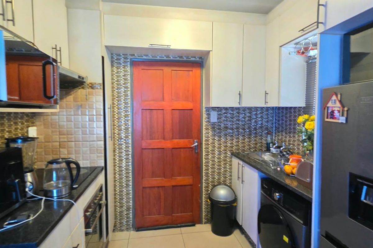 A functional kitchen featuring white cabinetry, tiled backsplash, integrated oven, and a timber door leading to the exterior.